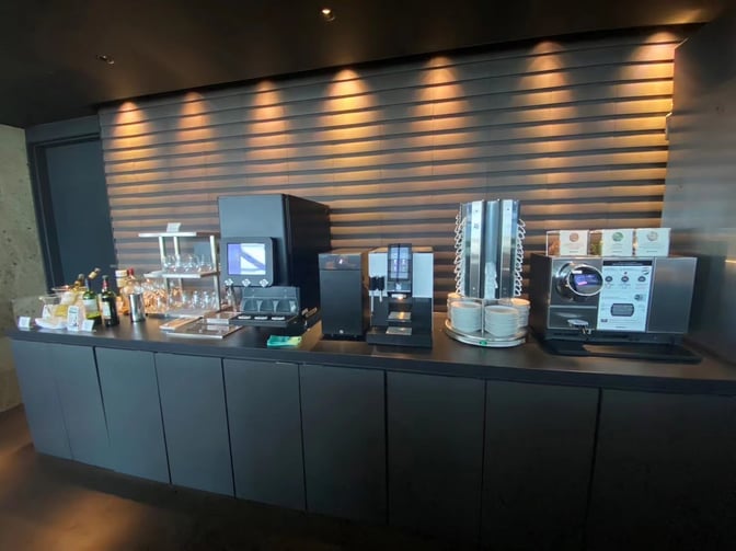 The Airside Lounge at Kansai International Airport features a self-serve beverage station with coffee machines, glassware, and assorted drinks.