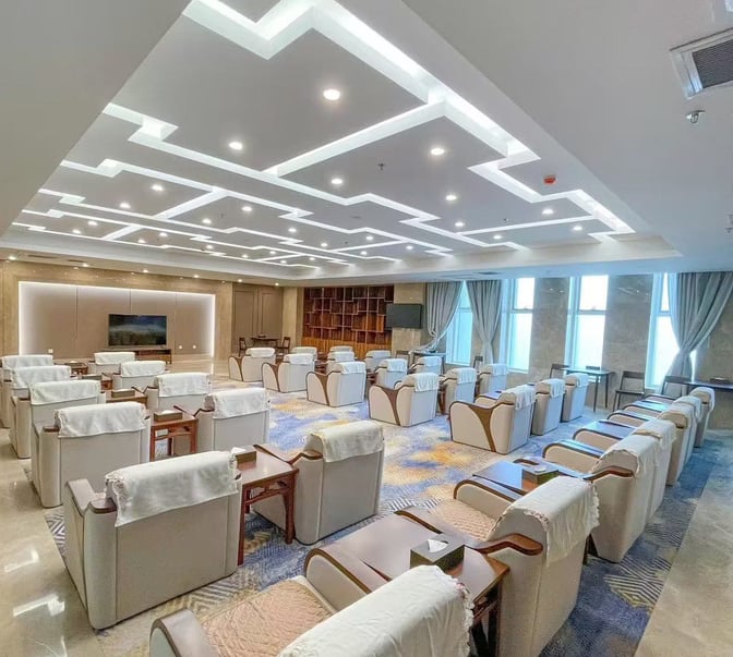 The seating area in Kashgar Airport's First Class Lounge features arranged armchairs with side tables, facing a large television screen.