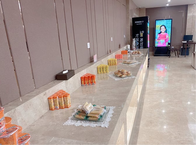 The food area in Kashgar Airport's First Class Lounge offers a selection of packaged snacks and beverages on a long counter.