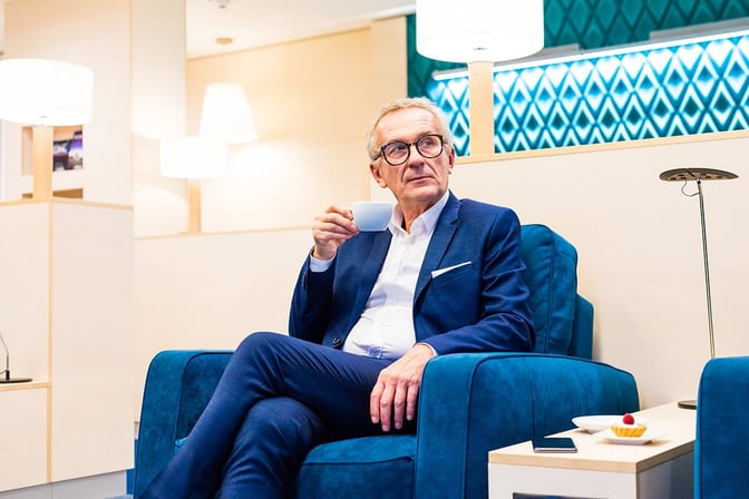 A guest enjoys a beverage in the seating area of Katowice Airport's Business Lounge, with nearby tables for snacks and devices.