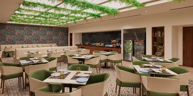 The dining area in the 080 Arrivals Lounge at Kempegowda Airport features arranged tables with place settings and a self-serve food station.