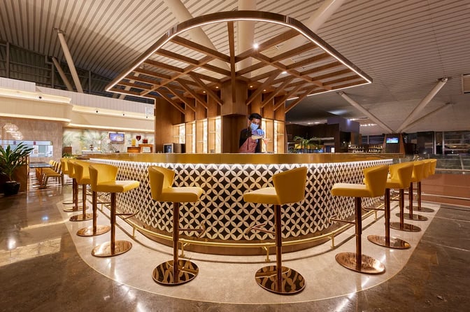 The bar at the 080 Domestic Lounge, Kempegowda Airport, features counter seating with a bartender preparing drinks.
