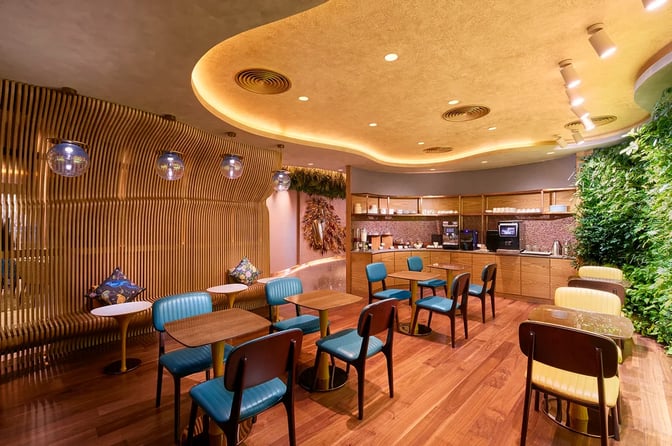 The lounge at Kempegowda Bangalore International Airport features seating with tables and a self-serve beverage station.