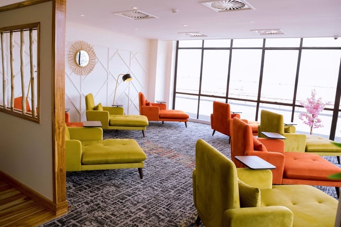 The Twiga Lounge at Kilimanjaro International Airport features comfortable chaise lounges with individual side tables, offering views through large windows.