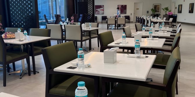 The Flynas Lounge at King Abdulaziz International Airport features a dining area with tables set with bottled water and napkins.