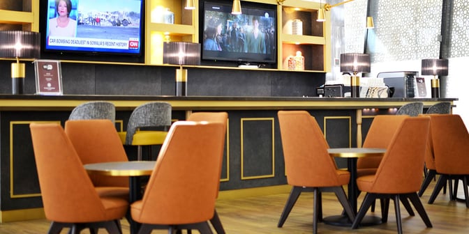 The Plaza Premium Lounge at King Abdulaziz International Airport features a seating area with tables and chairs facing a television.