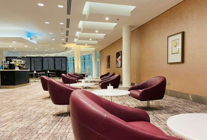 The Wellcome Lounge at King Abdulaziz International Airport features comfortable seating with round tables and a self-serve beverage station.