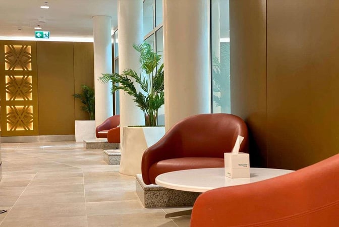 Seating area in the Wellcome Lounge at King Abdulaziz International Airport features round tables and chairs with nearby potted plants.