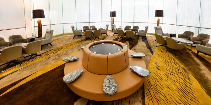 The seating area in the Plaza Premium Lounge at King Fahd International Airport features circular seating with integrated tables and armchairs.