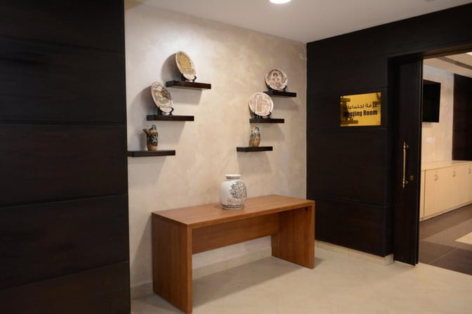 The meeting room entrance at Pearl Lounge, King Hussein International Airport, features decorative shelves with pottery and a wooden table.