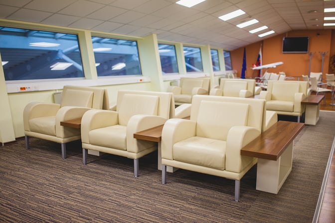The Kosice Business Lounge seating area features comfortable armchairs with attached side tables, offering views of the airport through large windows.