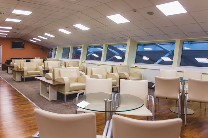 The Kosice Business Lounge at Kosice International Airport features comfortable seating with tables, offering views through large windows.