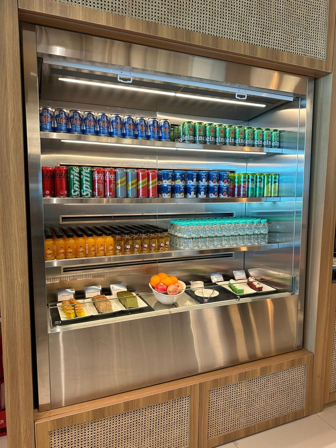 The self-serve beverage and snack station at Kota Kinabalu International Airport's Travel Club Lounge offers canned drinks, bottled juices, and assorted pastries.