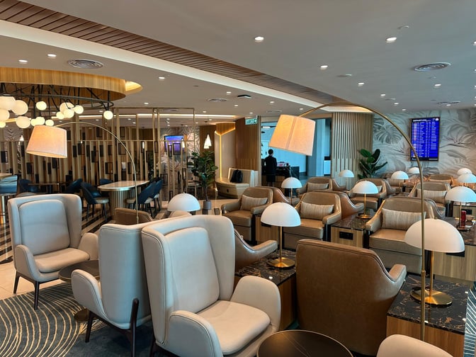 The Travel Club Lounge at Kota Kinabalu International Airport features comfortable seating with personal lamps and a view of the flight information screen.