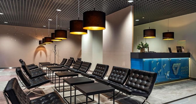 The Krakow Airport business lounge features a seating area with cushioned chairs and tables, adjacent to a reception desk.