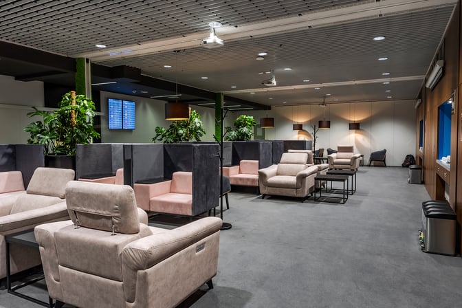 The Krakow Airport business lounge features comfortable seating areas with armchairs and semi-private booths, complemented by flight information screens.