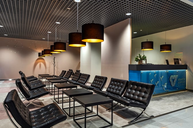The Krakow Airport Business Lounge features a seating area with leather chairs and tables, adjacent to a reception desk.