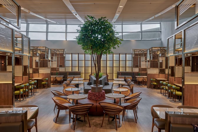 The seating area in Plaza Premium Lounge at Kuala Lumpur International Airport features round tables and chairs surrounding a central plant.