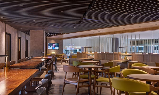 The seating area in Plaza Premium Lounge at Kuala Lumpur International Airport features tables and chairs with a television for entertainment.