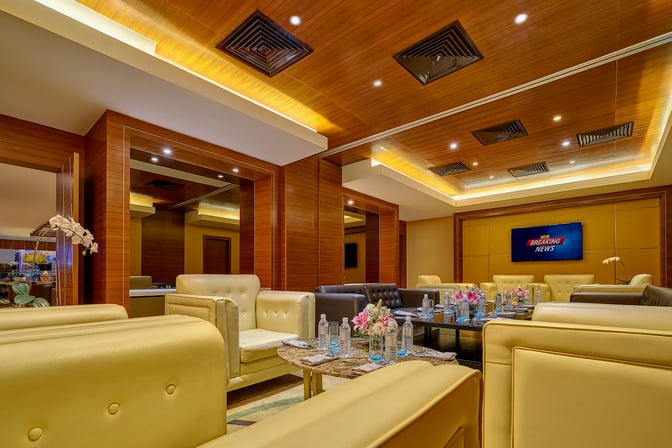 The Sky Suite Airport Lounge at Kuala Lumpur International Airport features comfortable seating with tables set for refreshments and a TV screen.