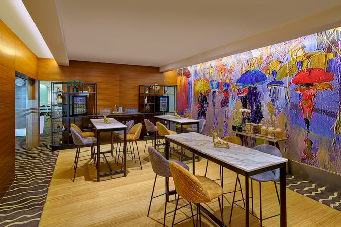 High tables and chairs in the Sky Suite Airport Lounge at Kuala Lumpur International Airport provide a casual seating area with snacks available.