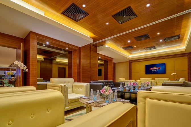 The Sky Suite Airport Lounge at Kuala Lumpur International Airport features comfortable seating with tables set for refreshments and a TV screen.