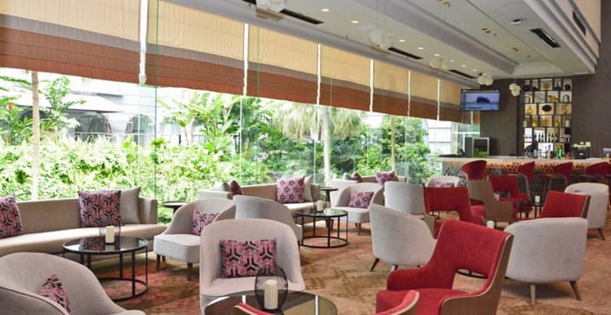 The seating area at Sphere Lounge, Kuala Lumpur International Airport, features a variety of chairs and tables with views of the garden.