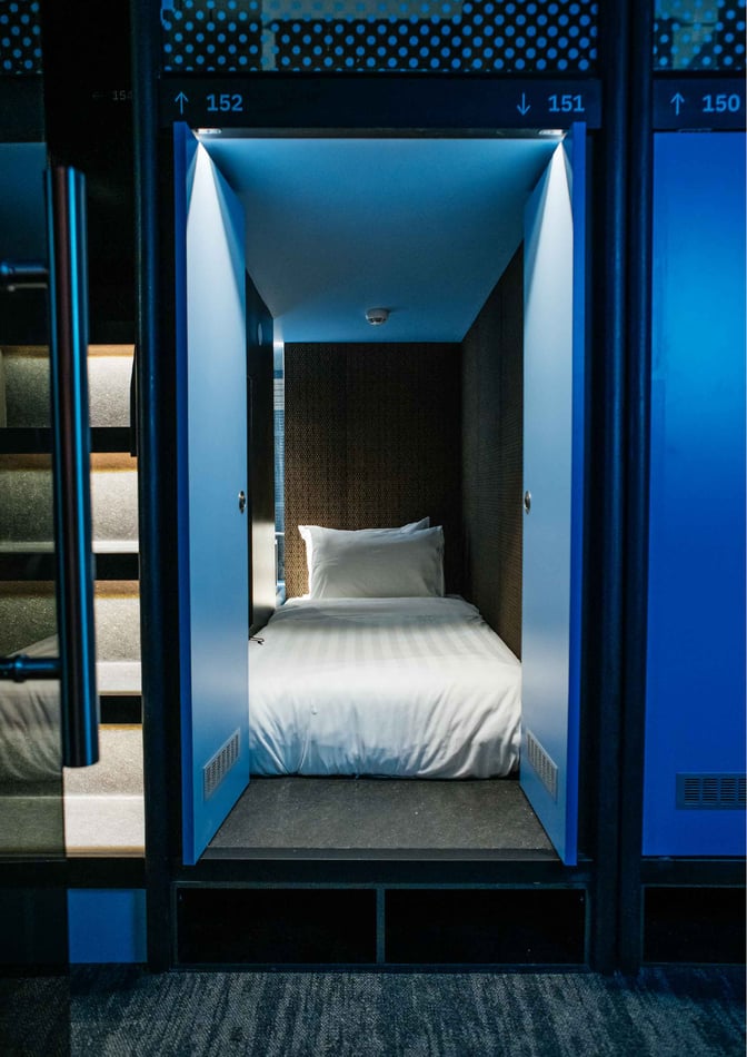 A sleeping pod at Capsule Transit KLIA 2 features a single bed with privacy doors, located airside at Kuala Lumpur International Airport.