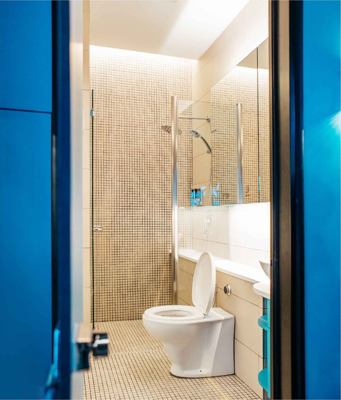The bathroom at Capsule Transit KLIA 2 features a toilet and shower area with tiled walls and a mirrored vanity.