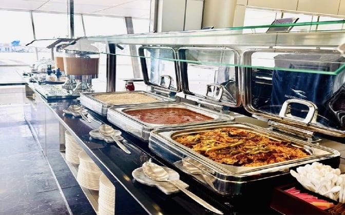 The Dasman Premier Lounge at Kuwait International Airport features a buffet with hot dishes and beverage dispensers for travelers.