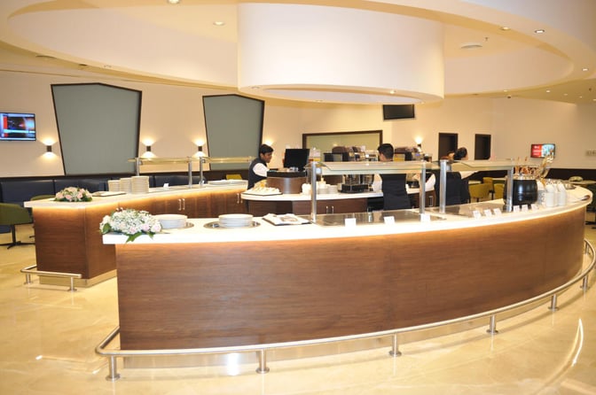 The Pearl Lounge at Kuwait International Airport features a staffed buffet area with self-serve stations and seating for dining.