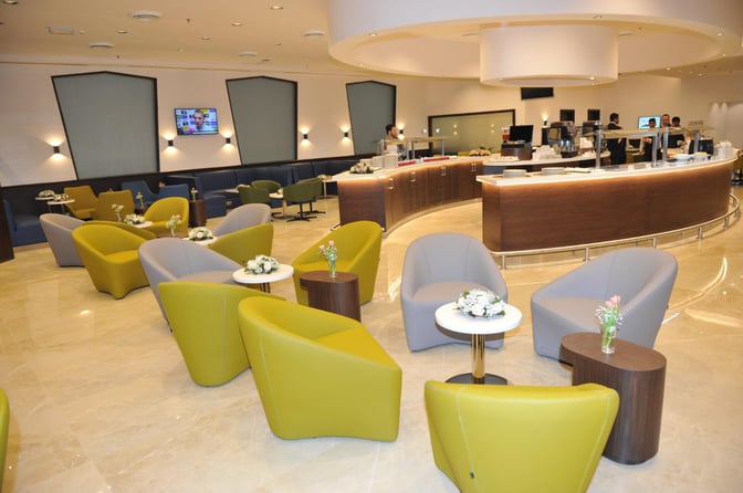 The Pearl Lounge at Kuwait International Airport features a seating area with armchairs and small tables, adjacent to a curved service counter.
