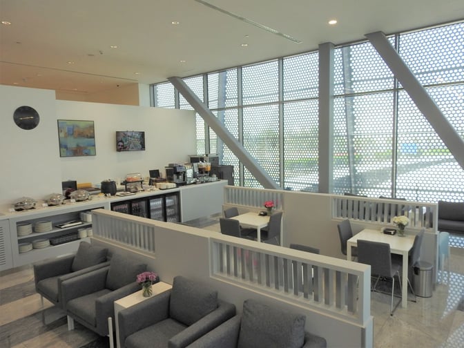 The Pearl Lounge at Kuwait International Airport features a self-serve food area with seating, offering various dining options and beverages.