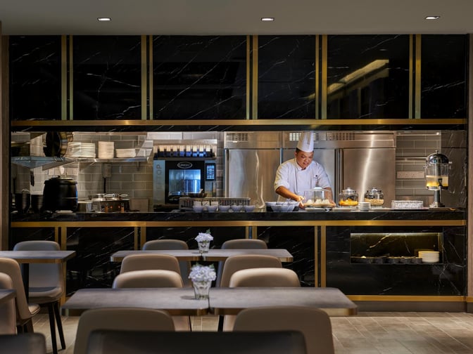 The dining area at Plaza Premium Lounge, Langkawi Airport, features a chef preparing food behind a counter with seating available.