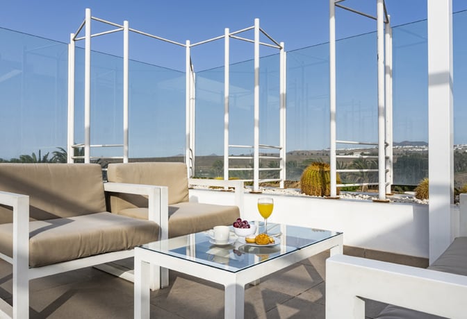 Outdoor seating at Sala VIP Guacimeta features cushioned chairs and a glass table with refreshments, offering views of the surrounding landscape.