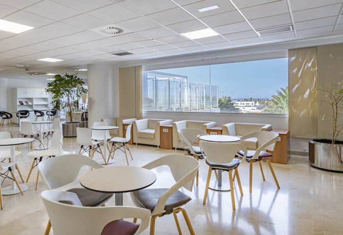 The seating area in Sala VIP Guacimeta at Lanzarote Airport features tables and chairs with views of the airport exterior.