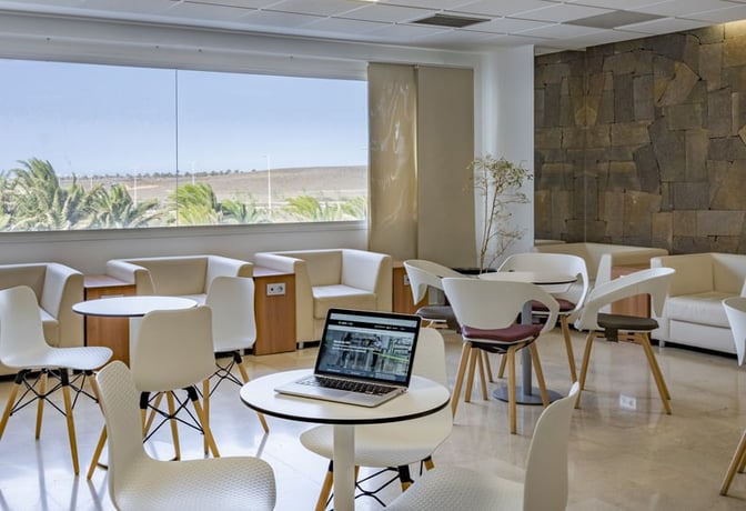 The seating area in Sala VIP Guacimeta at Lanzarote Airport features tables and chairs with views of the landscape outside.