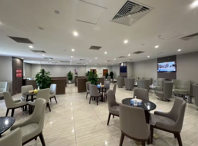 The First Class Lounge at Lhasa Gonggar Airport features seating areas with tables, chairs, and a display screen for flight information.