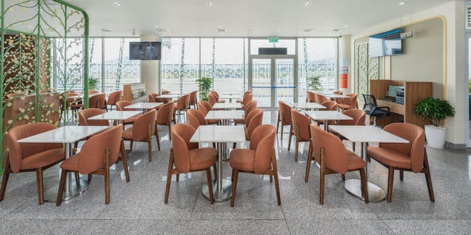 The seating area in SH Premium Lounge at Lien Khuong International Airport features tables and chairs with views of the tarmac.