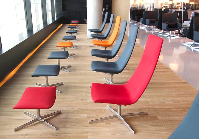 The seating area in the ANA Airport Lounge at Lisbon Portela Airport features modern chairs with footrests arranged along a windowed wall.