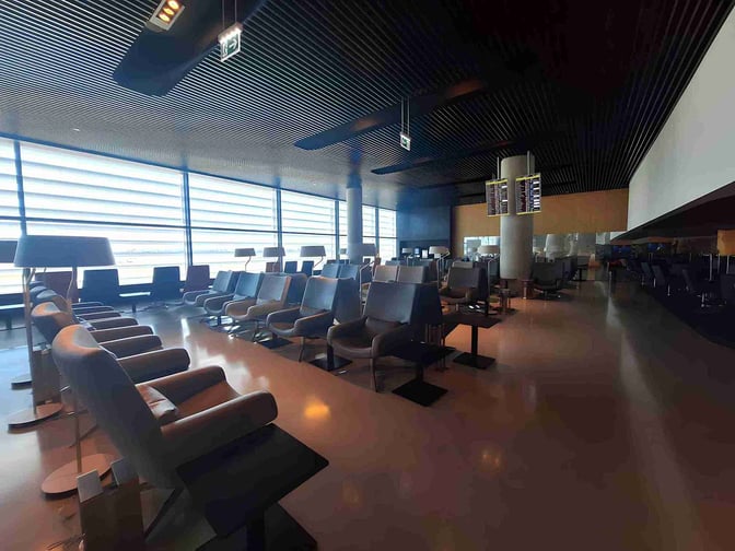 The ANA Airport Lounge at Lisbon Portela Airport features spacious seating with tables and a view of the tarmac.