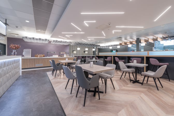 The Aspire Lounge at Liverpool John Lennon Airport features a spacious seating area with tables and chairs, adjacent to a self-serve food counter.