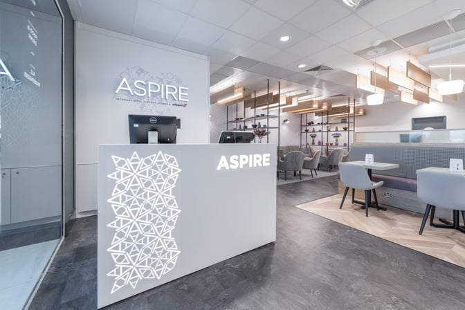 The Aspire Lounge at Liverpool John Lennon Airport features a reception desk and seating area with tables and chairs for passengers.