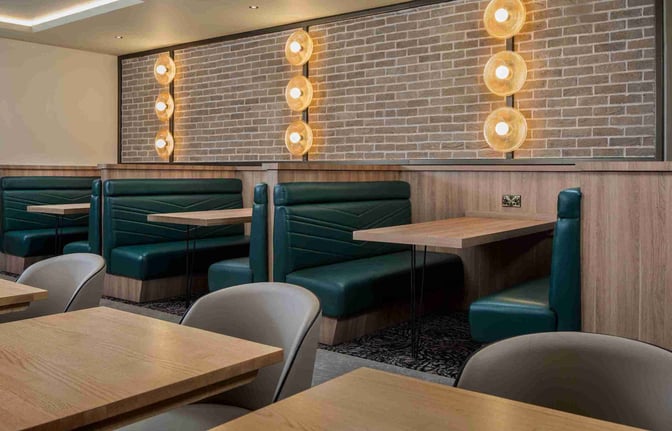 Booth seating in the Aspire Lounge at Liverpool John Lennon Airport offers semi-private dining with individual tables and wall-mounted lighting.