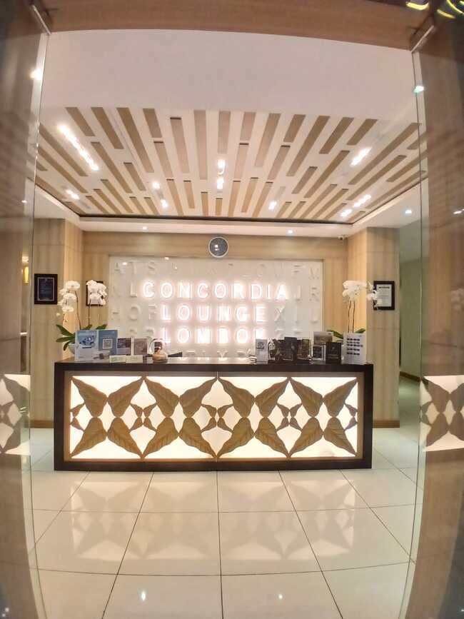 The entrance to Concordia Lounge at Lombok International Airport features a reception desk with informational brochures and decorative elements.