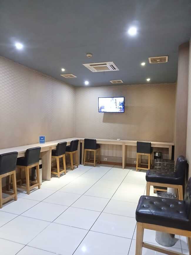 The Concordia Lounge at Lombok International Airport features a seating area with counter-height tables, chairs, and a wall-mounted television.
