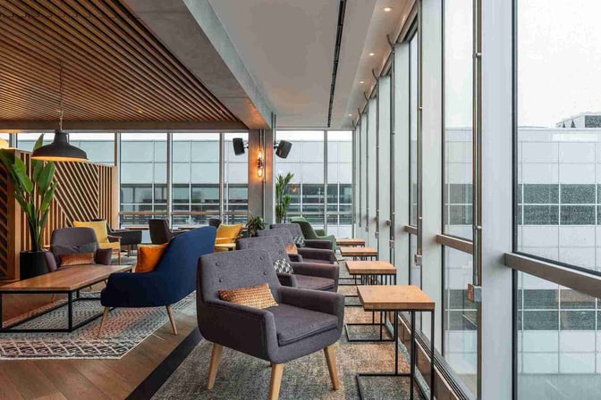 Seating area in My Lounge at London Gatwick Airport features comfortable chairs and tables with views of the airport through large windows.