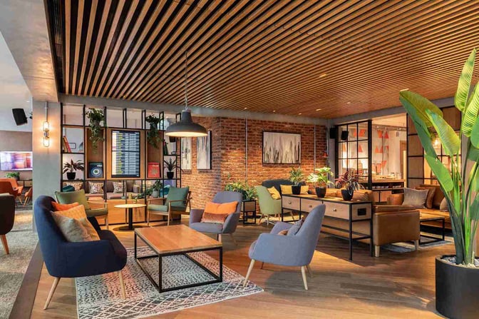 The seating area in My Lounge at London Gatwick Airport features comfortable chairs and tables, with a flight information display.
