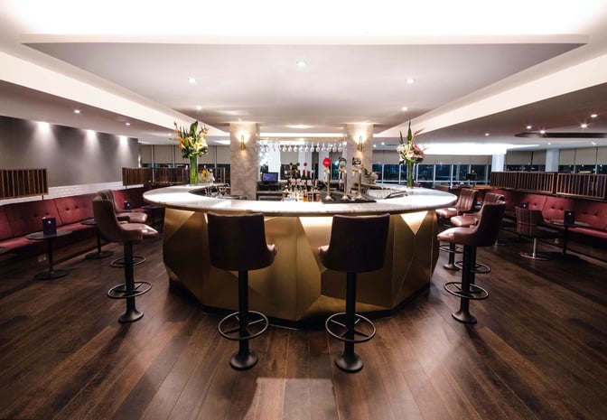 The No1 Lounge at London Gatwick Airport features a central bar with high stools and surrounding seating areas for travelers.