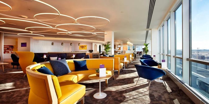 The Plaza Premium Lounge at London Gatwick Airport features spacious seating areas with tables, overlooking the airport through large windows.
